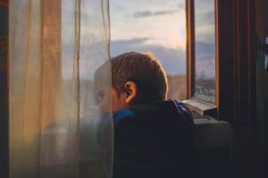 lonely boy gazing out a window at mountains