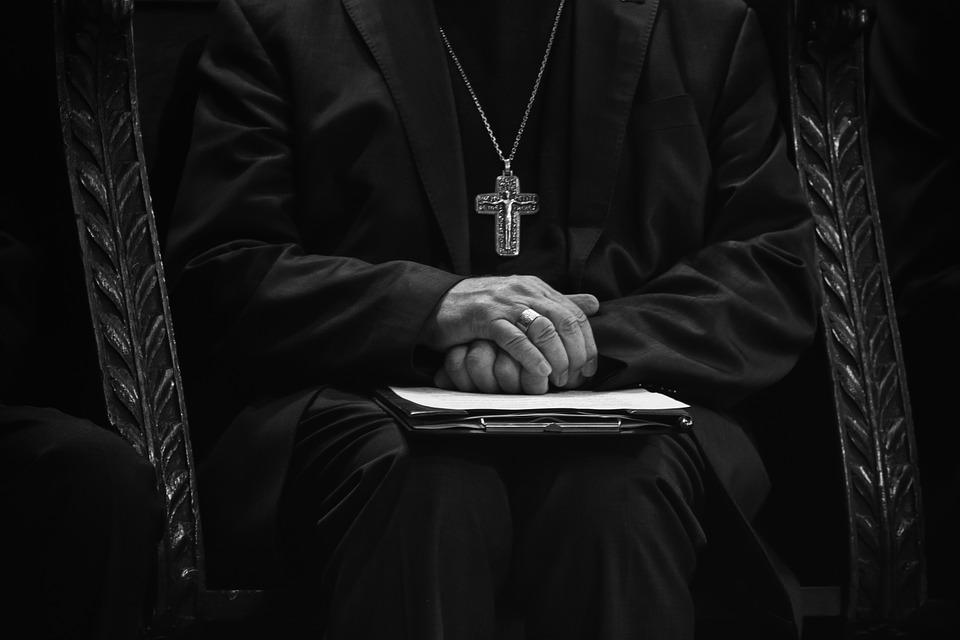 priest with hands crossed over bible